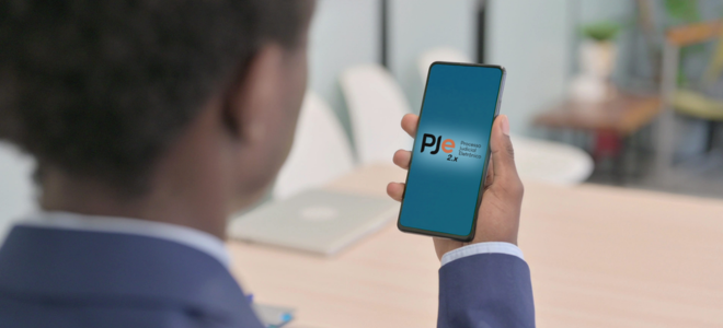 Imagem Foto mostrando a cabeça de uma pessoa de costas olhando para um celular, que fica localizado ao centro da foto, onde podemos ver na tela 